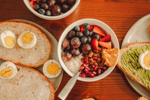 A fresh and vibrant breakfast flat lay featuring a yogurt bowl with fruits and toast with eggs and avocado.