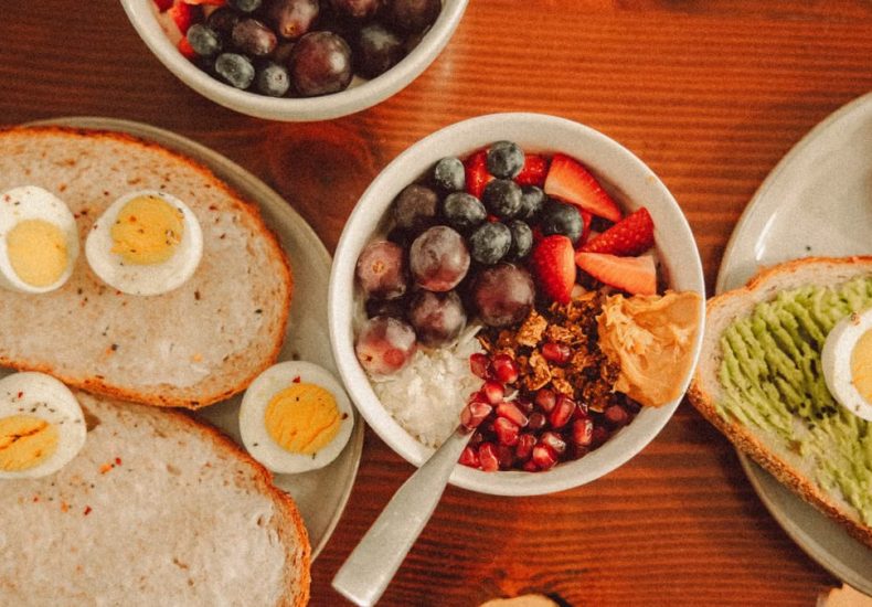 A fresh and vibrant breakfast flat lay featuring a yogurt bowl with fruits and toast with eggs and avocado.