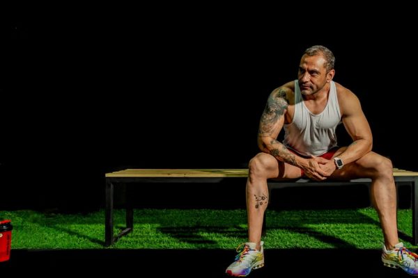 A muscular, tattooed man seated on a bench in a gym, depicting modern fitness lifestyle.